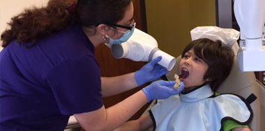 Pediatric dentist performing gentle teeth cleaning on young child